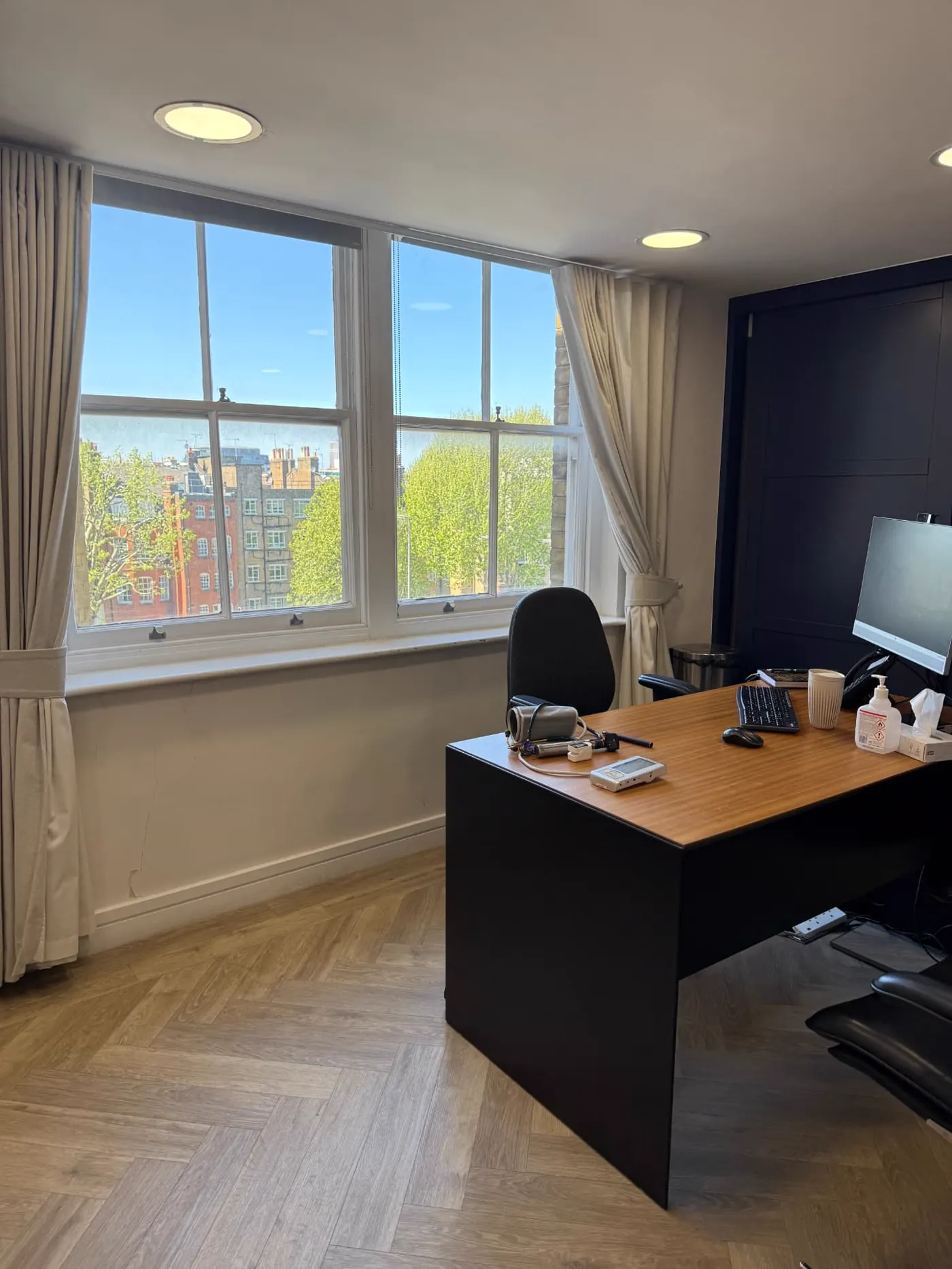 A light consulting room at Deia Health, 9 Harley Street, with blood pressure monitor on the desk